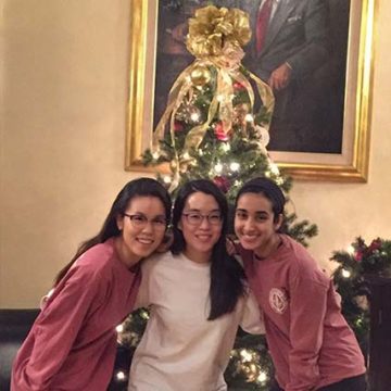 female students with arms around eachother in front of christmas tree