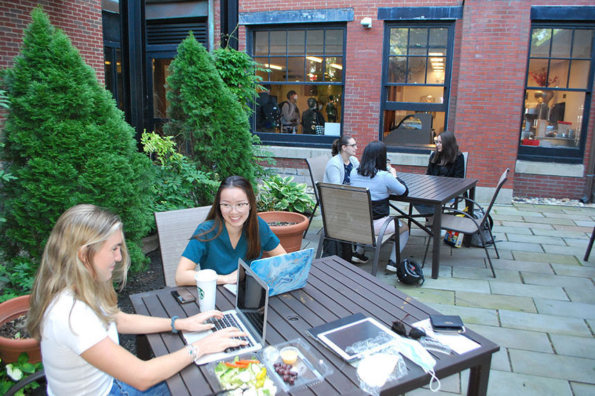 Two groups of students talking and studying in outdoor courtyard at Beacon Street location in the summer
