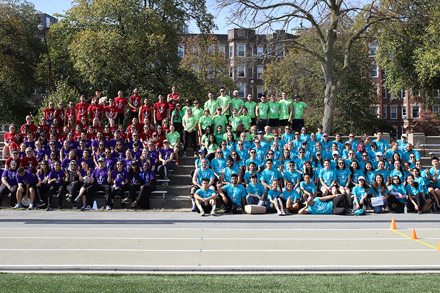 large group of students outside on stairs wearing different colored tshirts for student event