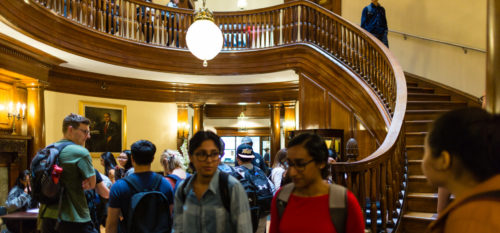A crowd of students in the Rotunda section of Beacon street, with a spiral staircase in the background.