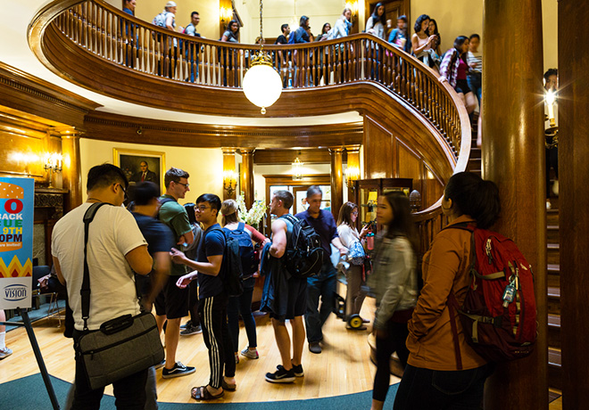 Many students in the rotunda of NECO, some walking down the spiral staircase.