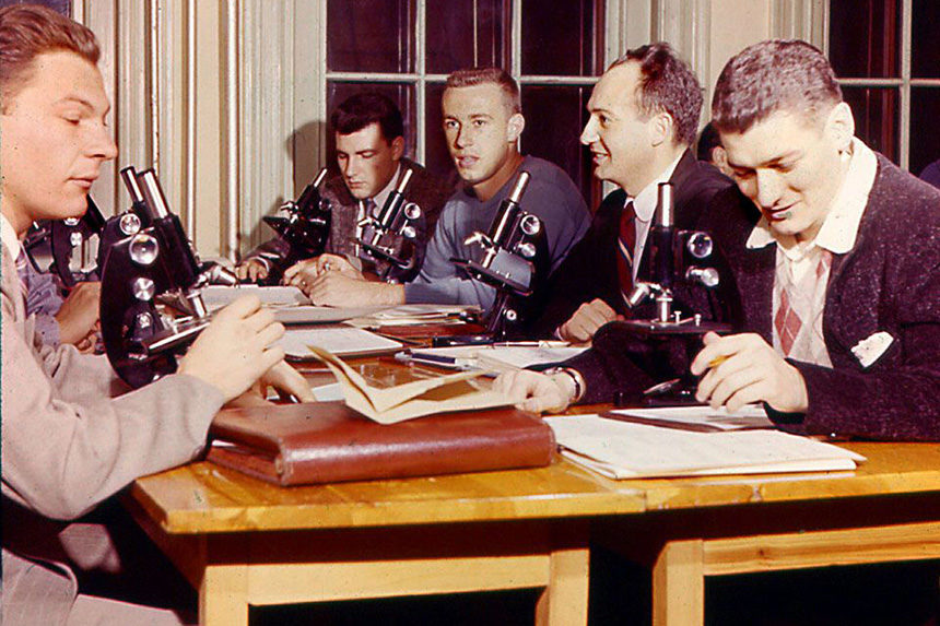 Students at a desk with microscopes in front.