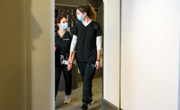 two students in scrubs talking and walking through doorway