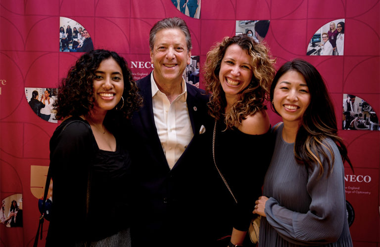 Four people standing in front of red backdrop smiling