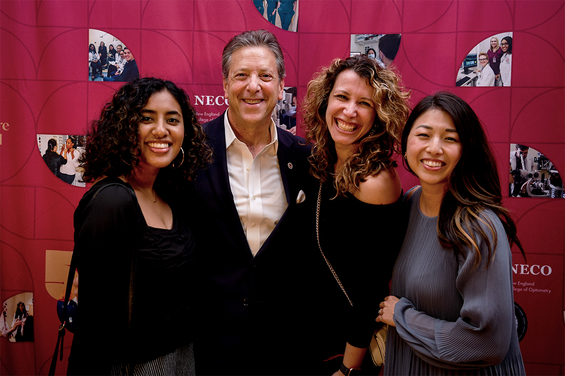 Four people standing in front of red backdrop smiling